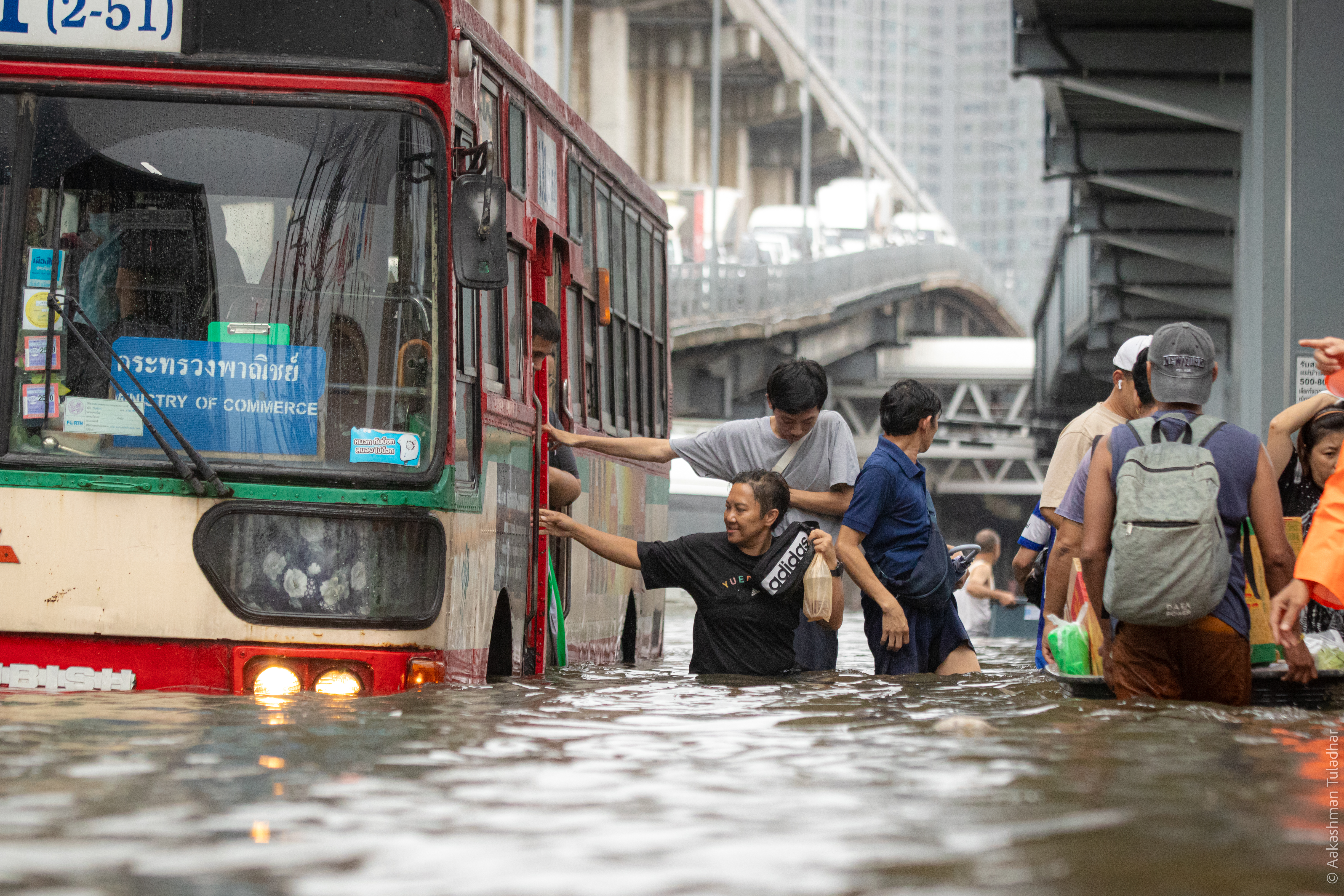 Commuters wading through flooded Bangkok street beside a bus