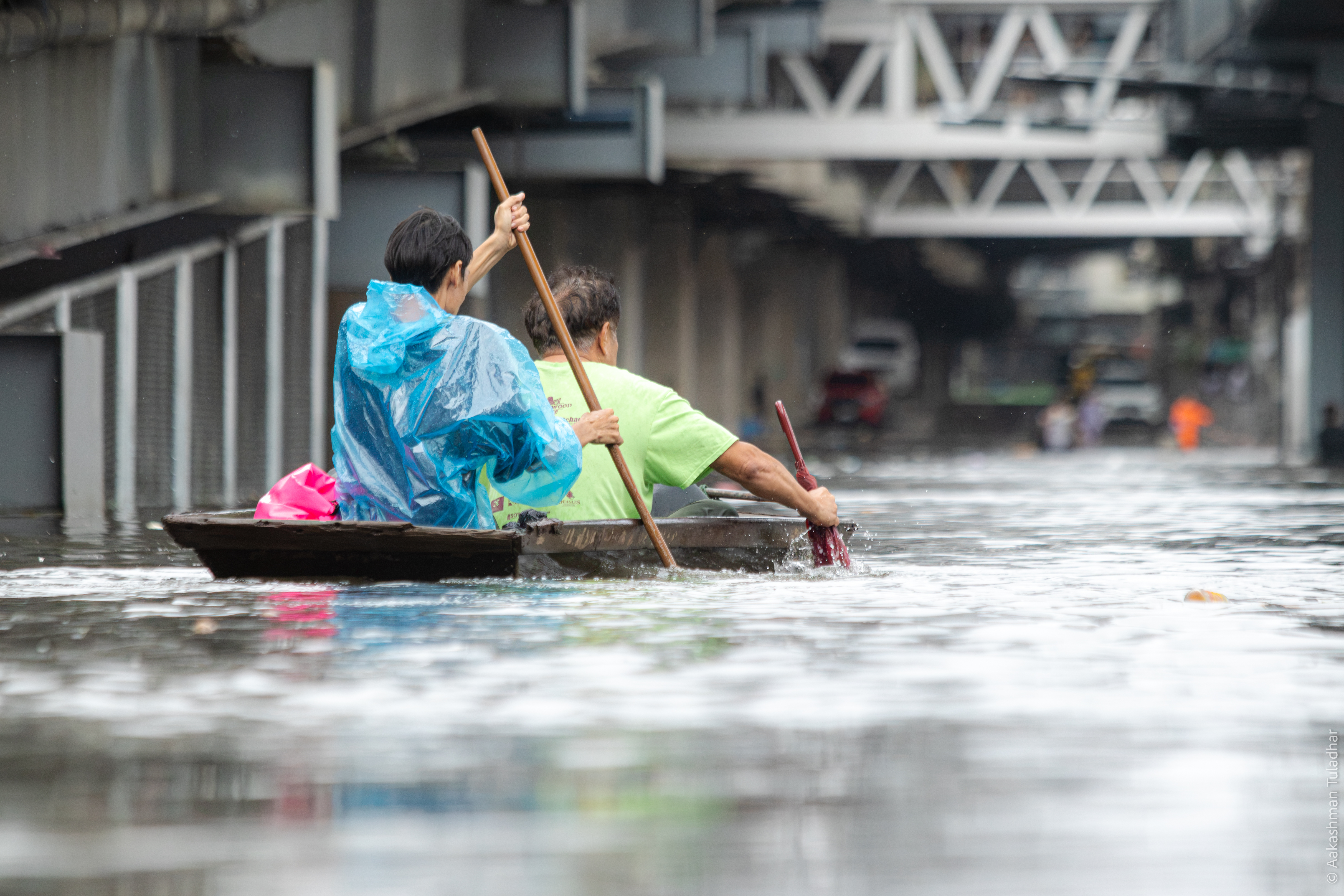 Two men paddling a wooden boat through flooded Bangkok streets