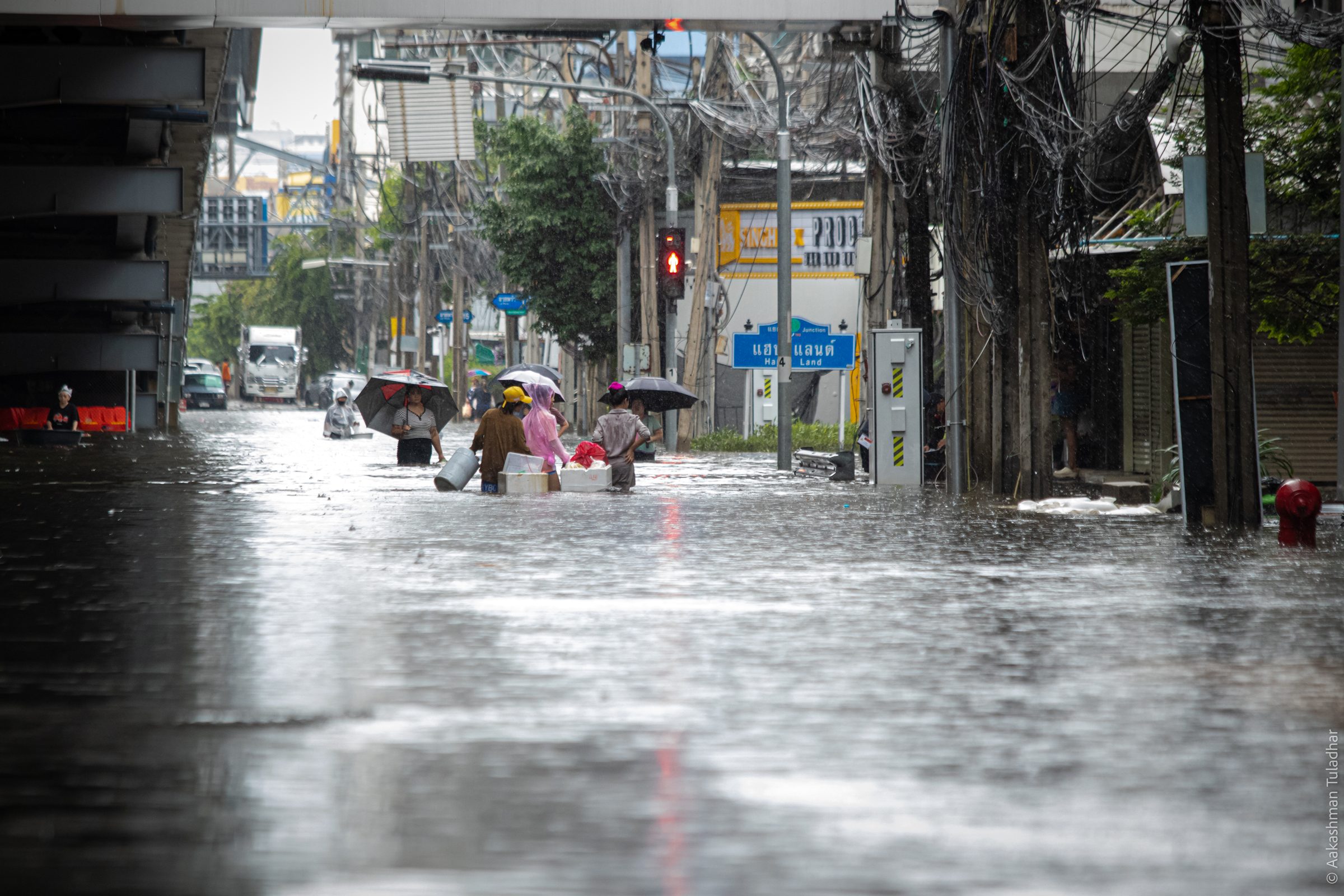 People wading through a flooded Bangkok street with umbrellas and boxes of belongings
