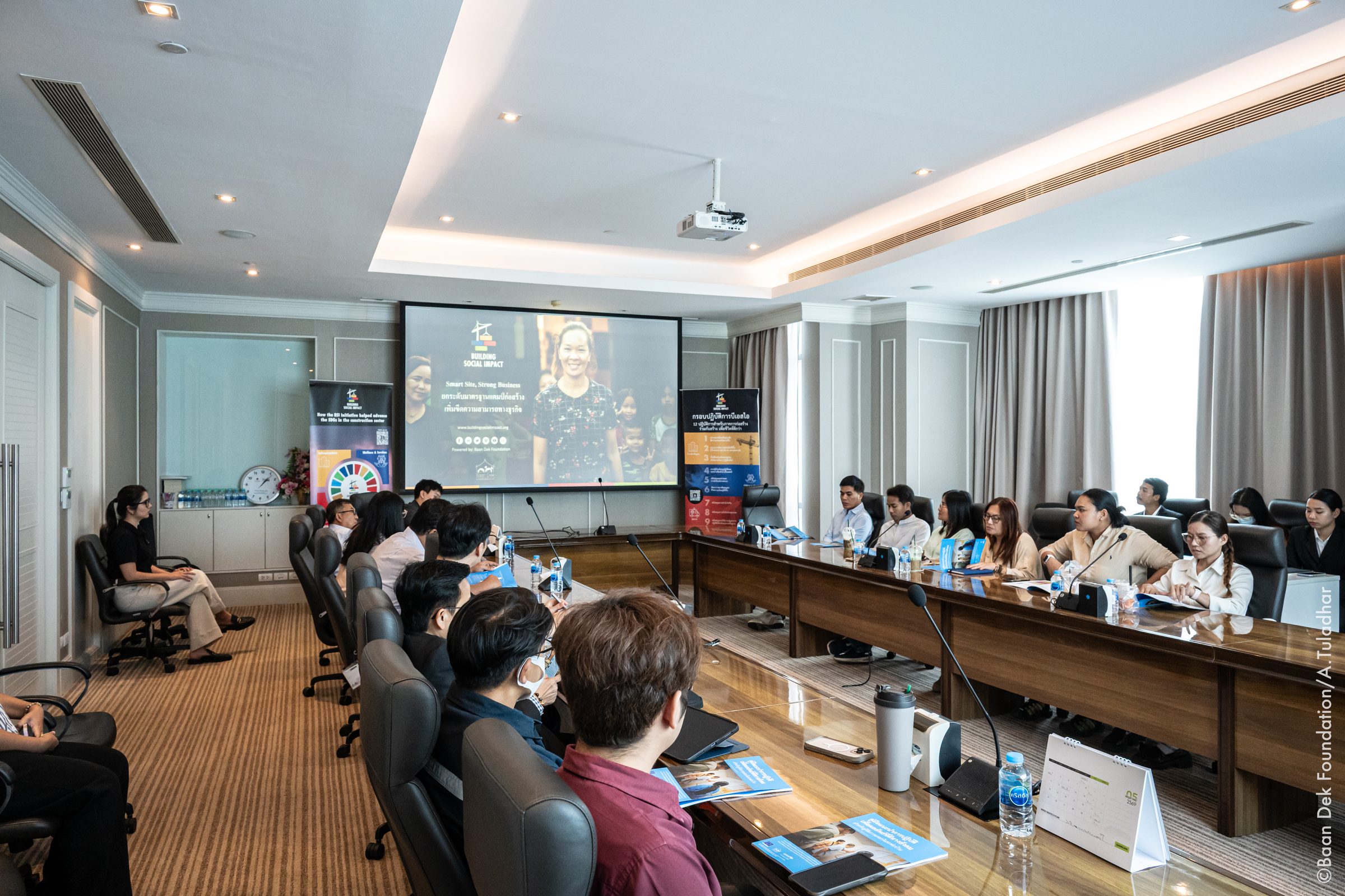 Participants at a meeting table facing a projected Building Social Impact presentation