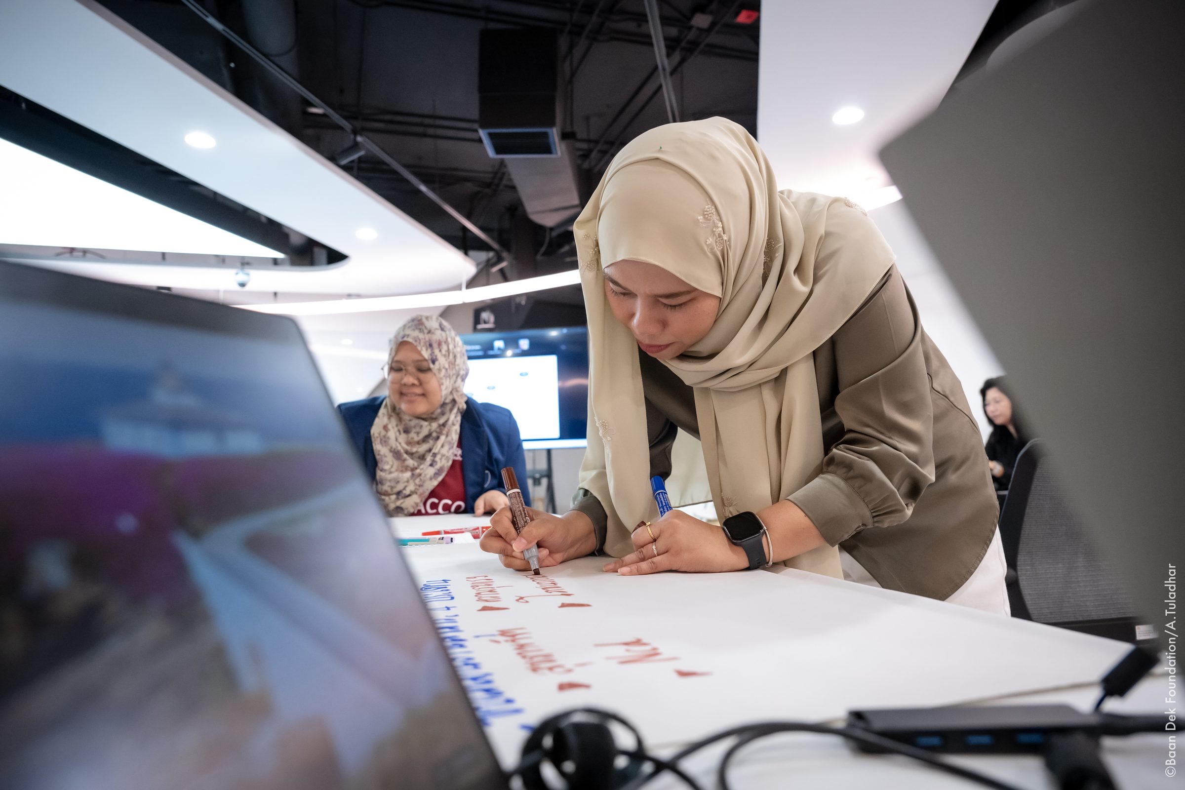 Woman in a hijab writing on a large sheet of paper during a workshop