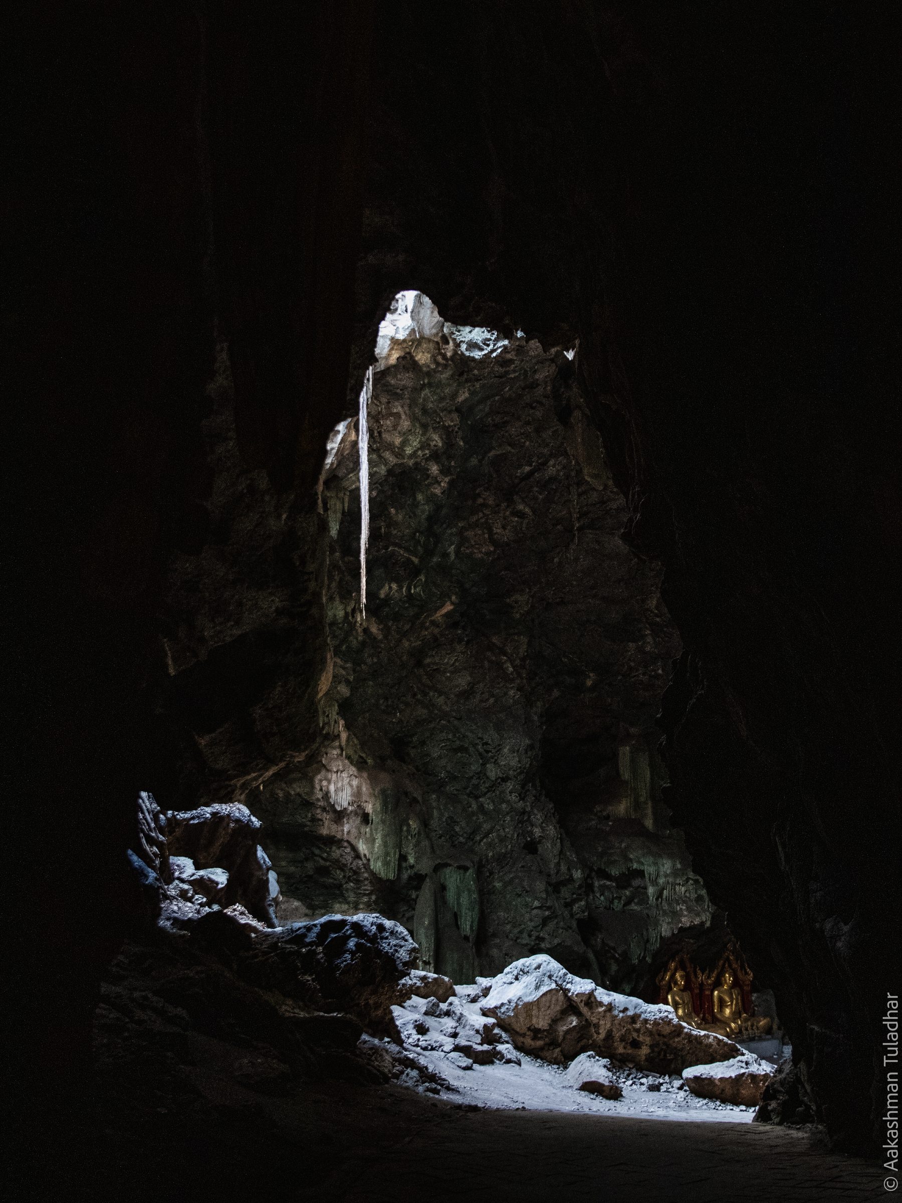 Sunlight falling into a dark cave where golden Buddha statues sit